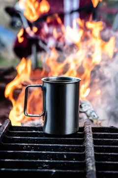 Coffee mug warming on grill over campfire flames