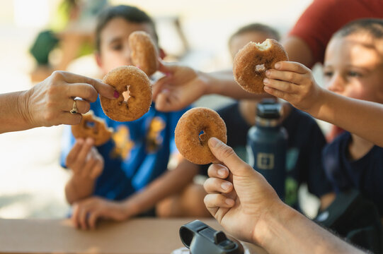 Group of kids toasting apple cider donuts at picnic table