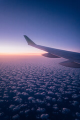 Fototapeta premium Airplane Wing Above Cloudscape at Sunrise – View from Window Seat