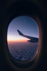 Fototapeta premium Airplane Wing Seen Through Window at Sunrise Above the Clouds