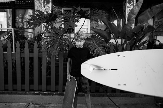 BW photo of boy with a skate board and surf board going by