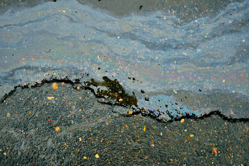Iridescent oil slick creating abstract rainbow patterns on wet asphalt with crack, showing liquid pollution and environmental concept