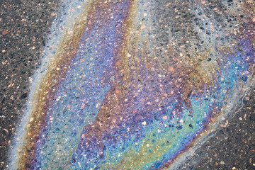 Oil slick creating a colorful, iridescent rainbow pattern on wet asphalt, representing environmental pollution, danger, and textured urban surface