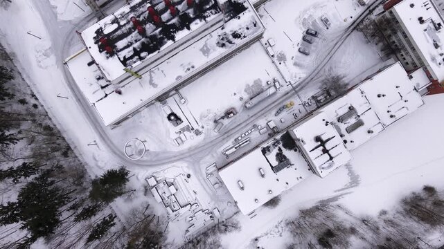 Aerial top-down drone shot of a tall industrial chimney and factory complex covered in snow during winter in Vilnius, Lithuania.