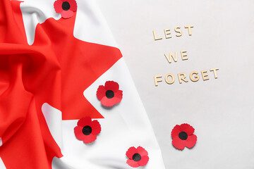Poppy flowers with flag of Canada and text LEST WE FORGET on grey background. Remembrance Day