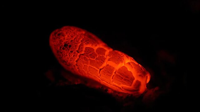 Glowing hot ember with cracks on dark background, a fiery texture