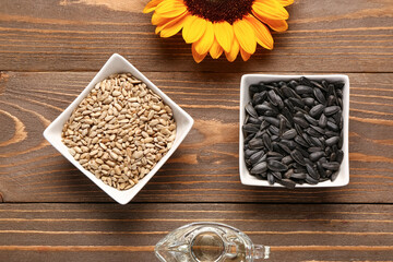 Sunflower, bowls with seeds and oil on wooden background