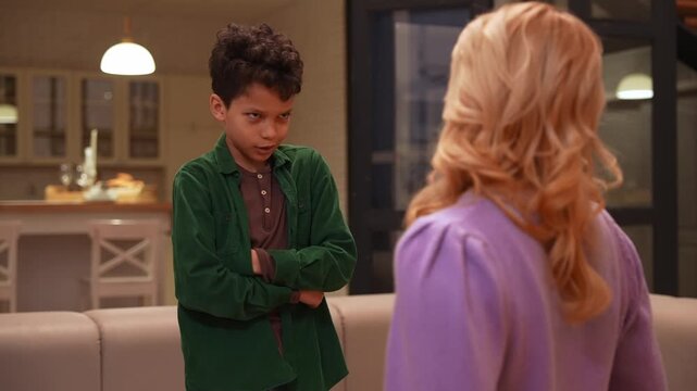 Disobedient preadolescent black boy with arms crossed having conflict with caring teenage babysitter, avoiding communication and punishment for bad deeds at home.