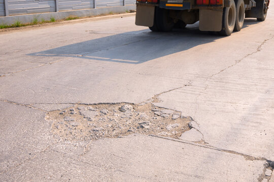 Pothole on damaged street surface with truck driving in background. Road maintenance and infrastructure problem concept