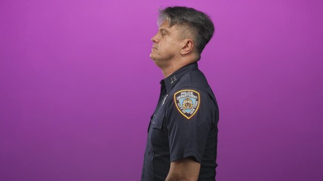 Man police officer in profile, middle aged with grey hair, wearing uniform with visible shoulder badge looking up against purple studio backdrop; solemn duty.