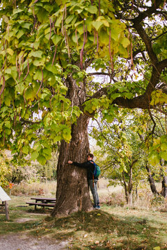 Teenage boy hugging large tree on hike with backpack
