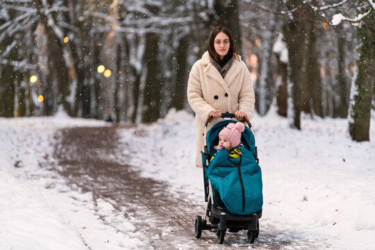 Woman pushing stroller with child on snowy path  park.