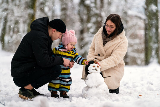 family and baby making small snowman in winter park
