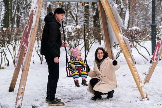 Zoomer parents push baby on swing at playground in park