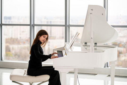 teenage girl plays the piano in a large white hall
