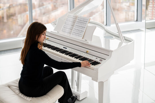 teenager is playing white piano with view of city from above.