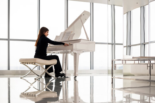 young girl is playing the piano in bright room with large window.