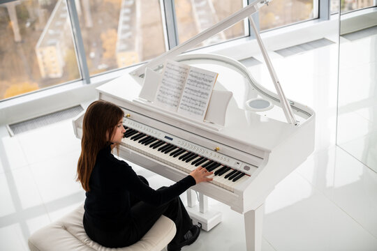 teenager is playing white piano with view of city from above.