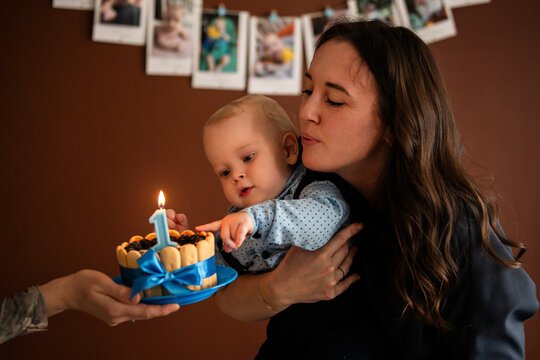 mother holds boy celebrating  first birthday with small cake