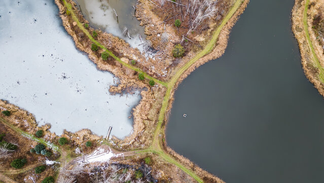 Top-down aerial view of frozen and partially frozen ponds with trails