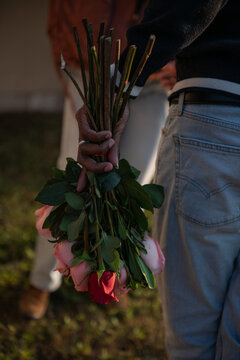 man's hand holds bouquet of red and pink roses
