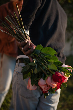 man's hand holds bouquet of roses behind his back