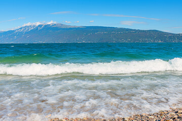 Breaking waves on the beach of Toscolano, Lake Garda, view towards Monte Baldo, italy
