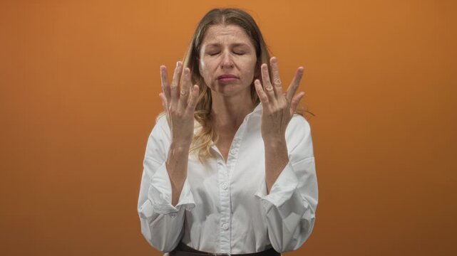 Woman pressing hands to eyes rubbing nose bridge in studio with orange wall wearing white shirt; fatigue recovery.
