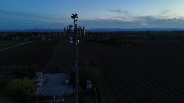 Aerial shot captures a telecommunication cell tower in silhouette against the stunning blue twilight sky, showcasing the countryside and mountain range in the distance