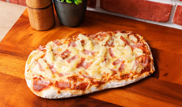 Blended culture traditional pinsa romana hawaiian pizza square shaped toppings with ham pineapple cheese golden yellow on wooden cutting board and brick wall tasty food fresh delicious gourmet cuisine