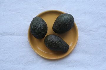three avocados on an orange plate on a white background. healthy vegetables .