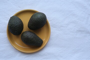 three avocados on an orange plate on a white background. healthy vegetables .