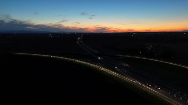 Aerial footage of a tall telecommunication tower equipped with antennas and satellite dishes, transmitting signals against a clear dark blue sky at dusk in a rural landscape