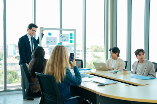 Business presentation in modern meeting room with large windows. Team reviewing analytics charts and discussing company performance. Leadership, collaboration, data driven decision making.