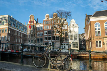 Classic bicycle leans on the seraphina van braziliebrug railing above a tranquil amsterdam canal, framed by gabled houses and historic architecture under a clear blue sky