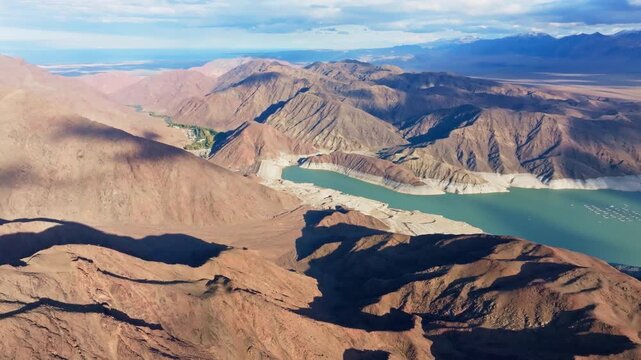Aerial view captures vast Orto Tokoy reservoir with dam amidst arid mountains. Small buildings dot the valley, enhancing peaceful, remote atmosphere.