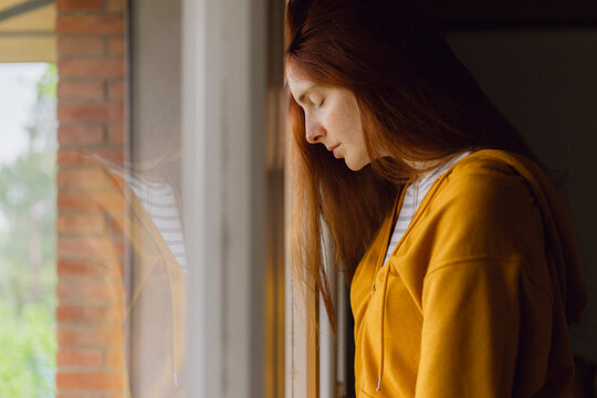 Redheaded woman with eyes closed leaning against window