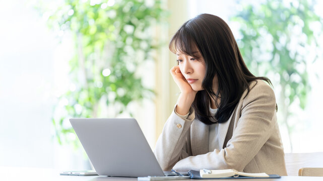 ノートパソコンを見ながら頬杖をつく女性ビジネスパーソン, Businesswoman resting her cheek on hand while looking at laptop