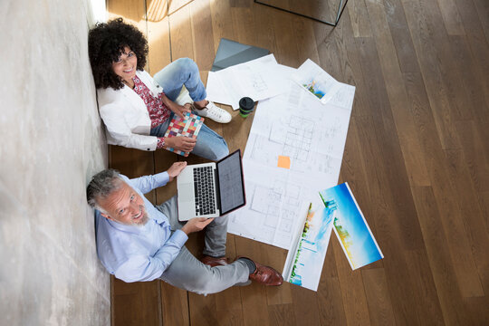 Businessman and businesswoman sitting on the floor in a loft working with laptop and documents