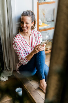 Laughing woman sitting on the floor at home with cell phone