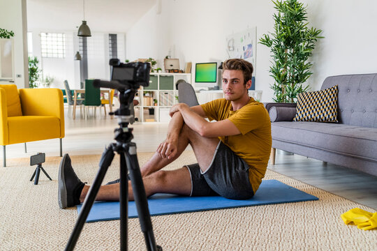 Fitness trainer recording exercise on camera while sitting on mat at home