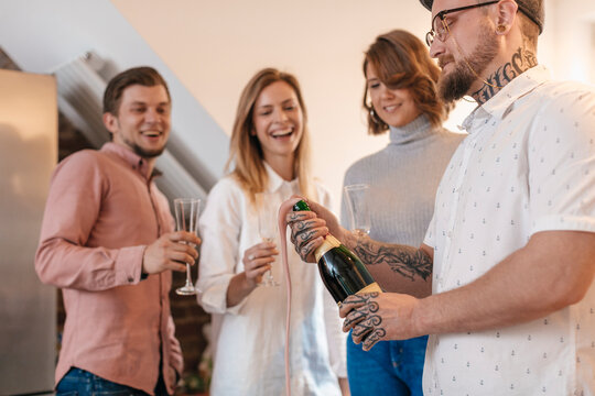 Man opening Champagne bottle while his friends watching