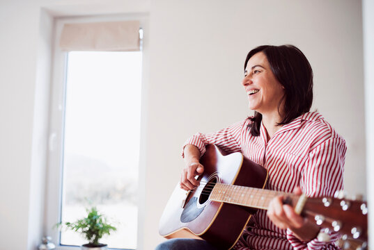 Happy mature woman playing guitar at home