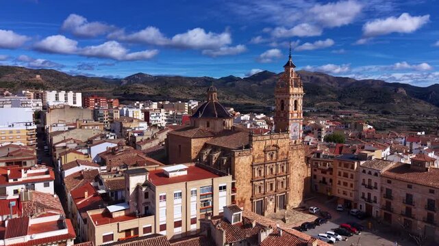 Detailed aerial view of Iglesia Nuestra Senora de los Angeles in Chelva, Spain, highlighting baroque architecture, bell tower, tiled dome, and surrounding historic rooftops