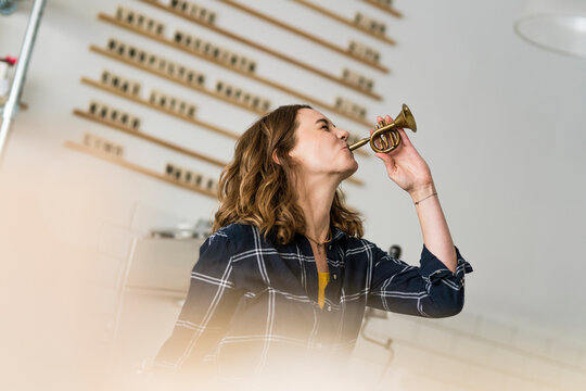 Young woman blowing toy trumpet in her coffee shop