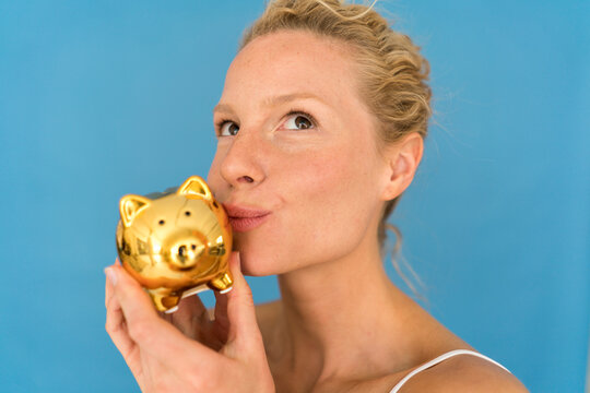 Portrait of blond woman kissing golden piggy bank
