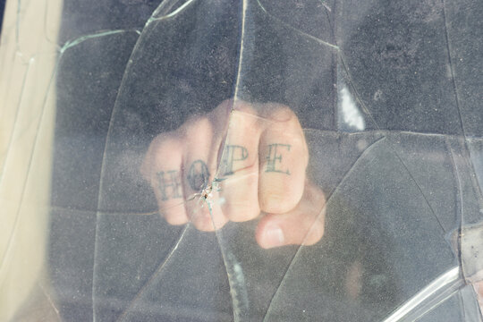 Fist of a young man with HOPE tattoo behind broken windscreen on a scrapyard
