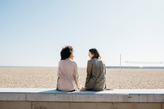 Back view of two friends sitting on the promenade enjoying leisure time