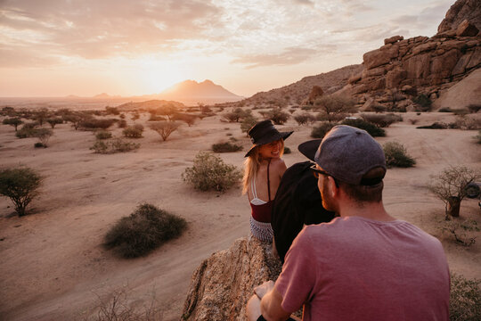 Namibia, Spitzkoppe, friends sitting on a rock at sunset