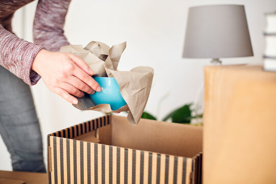 Close-up of woman unpacking cardboard box in new home taking out bowl